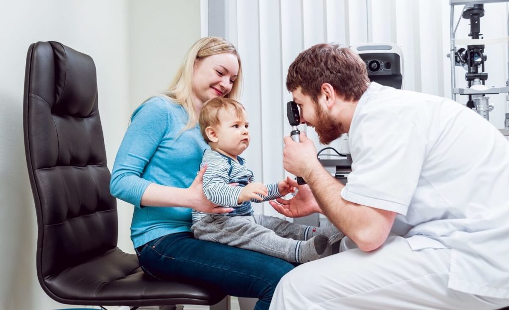 A mother holding her baby while the doctor examines the baby's eyes.