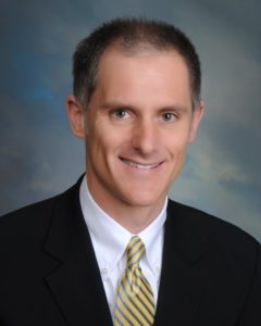 Board member, Joseph P. Gale. He is wearing a black blazer over a white shirt and yellow and grey tie.
