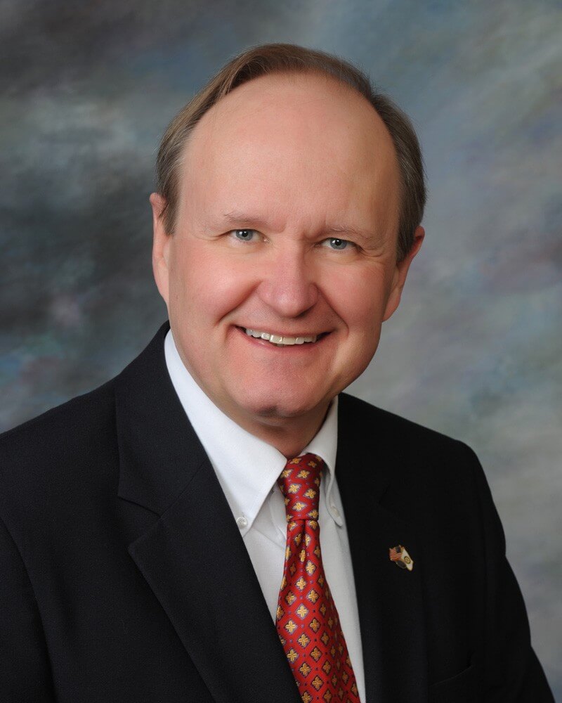 Board member, Thomas P. Webb. He is wearing a black blazer with a white shirt and a red and yellow tie.