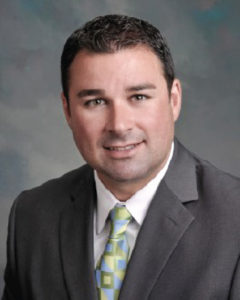 Gary Heenan wearing a grey suit with a white shirt and blue and green tie